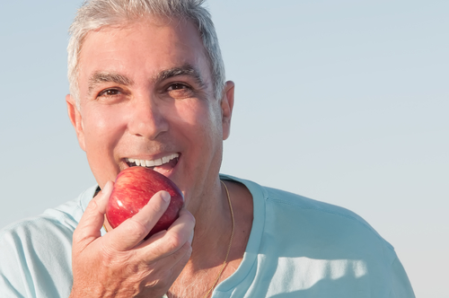 happy older man eating apple without denture problems