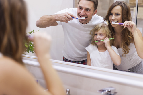 mother father and daughter brushing their teeth together