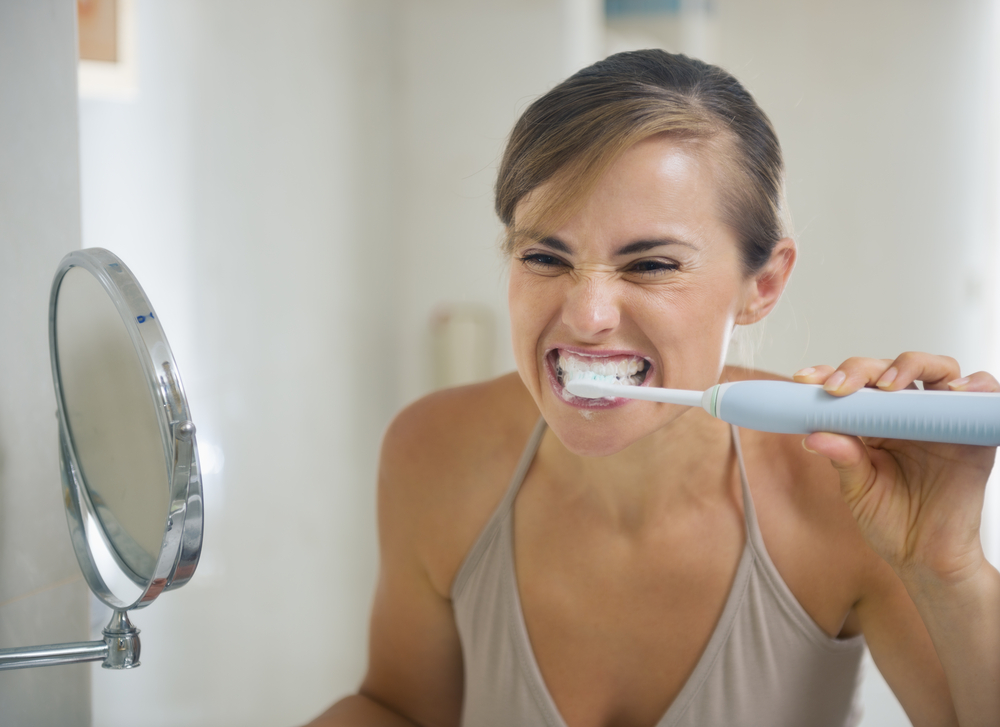 young woman brushing her teeth too aggressively