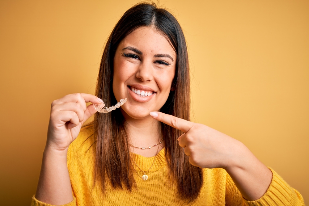 young woman holding invisalign aligner and smiling