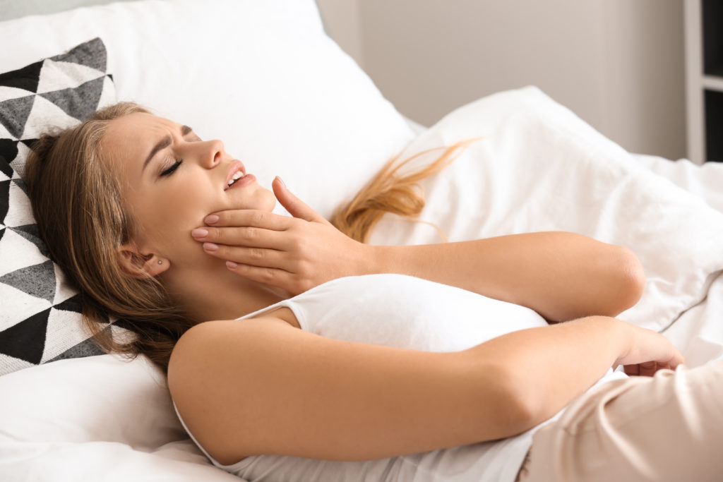 Woman waking up in bed with jaw pain.
