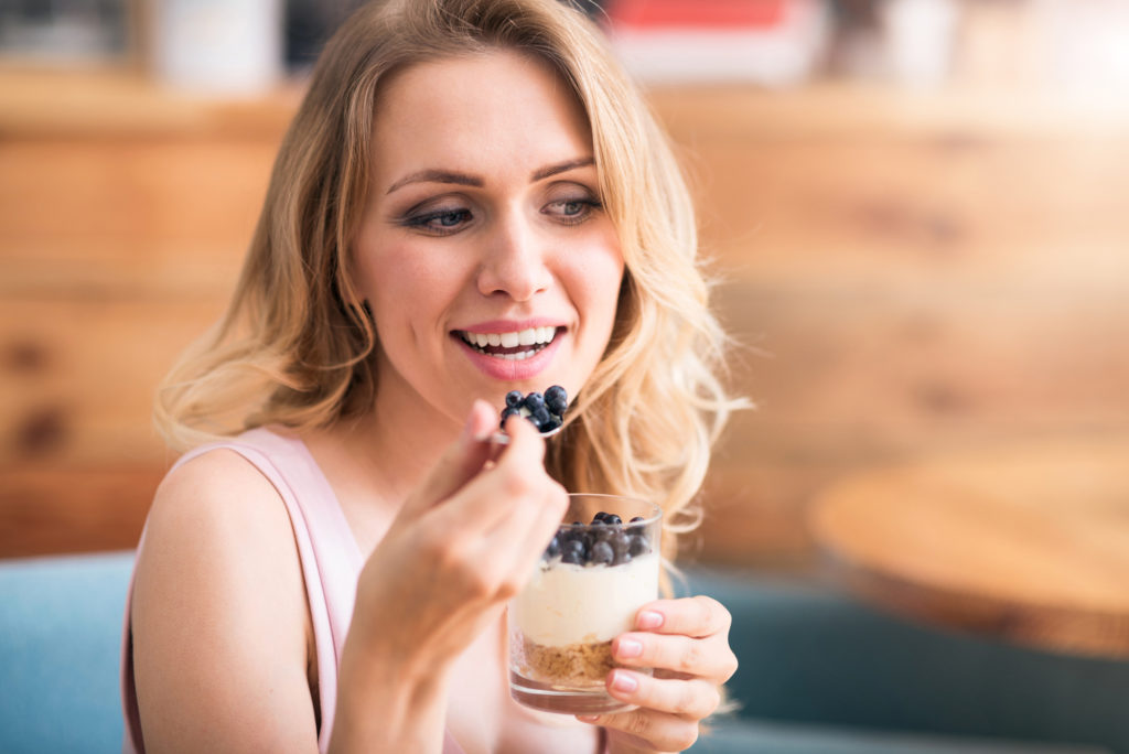 Woman with healthy white teeth eating berries and yogurt.