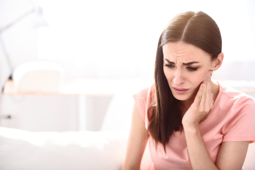 Woman holding her jaw and having jaw pain. 